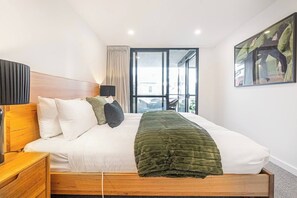 Une chambre dâhĂŽtel avec un lit, une tĂȘte de lit en bois, une table de chevet, une lampe, une fenĂȘtre avec des rideaux et un tableau au mur.