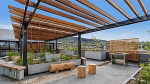 Une terrasse sur le toit agrémentée d’une pergola en bois, de sièges, de jardinières et offrant une vue sur la ville.
