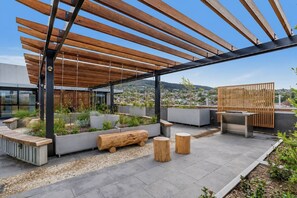 Eine Dachterrasse mit Holz-Pergola, Sitzgelegenheiten, Pflanzgefäßen und Blick auf die Stadt.
