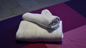 A folded white towel on a bed with a purple and red striped bedspread. - Mosaico (Pompei)