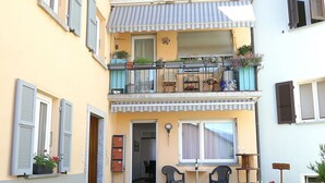 A two-story building with a balcony, a small outdoor seating area, and a door leading to an interior space. - Beautiful apartment for 5 guests with WIFI, TV and patio (Lodrino)