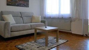 A living room with a sofa, a small table, a painting, and a window with curtains. - Beautiful apartment for 5 guests with WIFI, TV and patio (Lodrino)