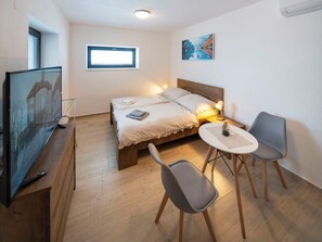 A bedroom with a bed, bedside table, chairs, a TV, a window, and a painting on the wall.
