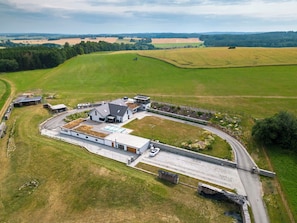 An aerial view of a rural property with a large building, a paved driveway, and surrounding fields.