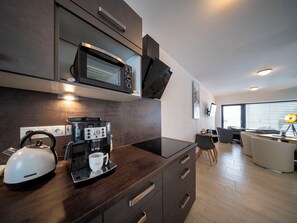 A modern kitchen with a microwave, coffee maker, kettle, and a dining area with a table and chairs.