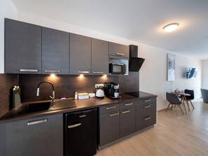 A modern kitchen with dark cabinets, a built-in microwave, a coffee machine, and a dishwasher.