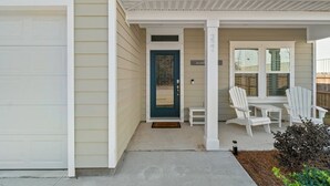 A house with a garage, a front door, a porch with white chairs, and a small garden area. - Walk to Beach, Golf Cart Included, Near Rosemary (Panama City Beach)