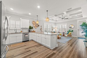 A modern kitchen with white cabinets, a built-in island, wooden flooring, pendant lighting, and a ceiling fan. - Walk to Beach, Golf Cart Included, Near Rosemary (Panama City Beach)