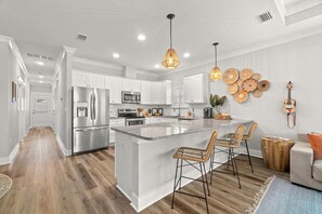 A modern kitchen with white cabinetry, stainless steel appliances, and a central island with bar stools. - Walk to Beach, Golf Cart Included, Near Rosemary (Panama City Beach)