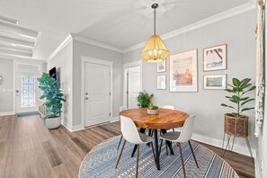 A dining area with a round wooden table, white chairs, a hanging light fixture, and a patterned rug. - Walk to Beach, Golf Cart Included, Near Rosemary (Panama City Beach)