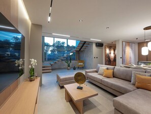 Ein modernes Wohnzimmer mit einer Couch, einem Couchtisch und einem Fernseher. Eine Treppe führt zu einer erhöhten Ebene.