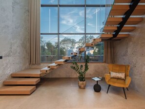 Ein modernes Interieur mit einer Holztreppe, einem Blumentopf, einem kleinen Tisch und einem gelben Sessel.