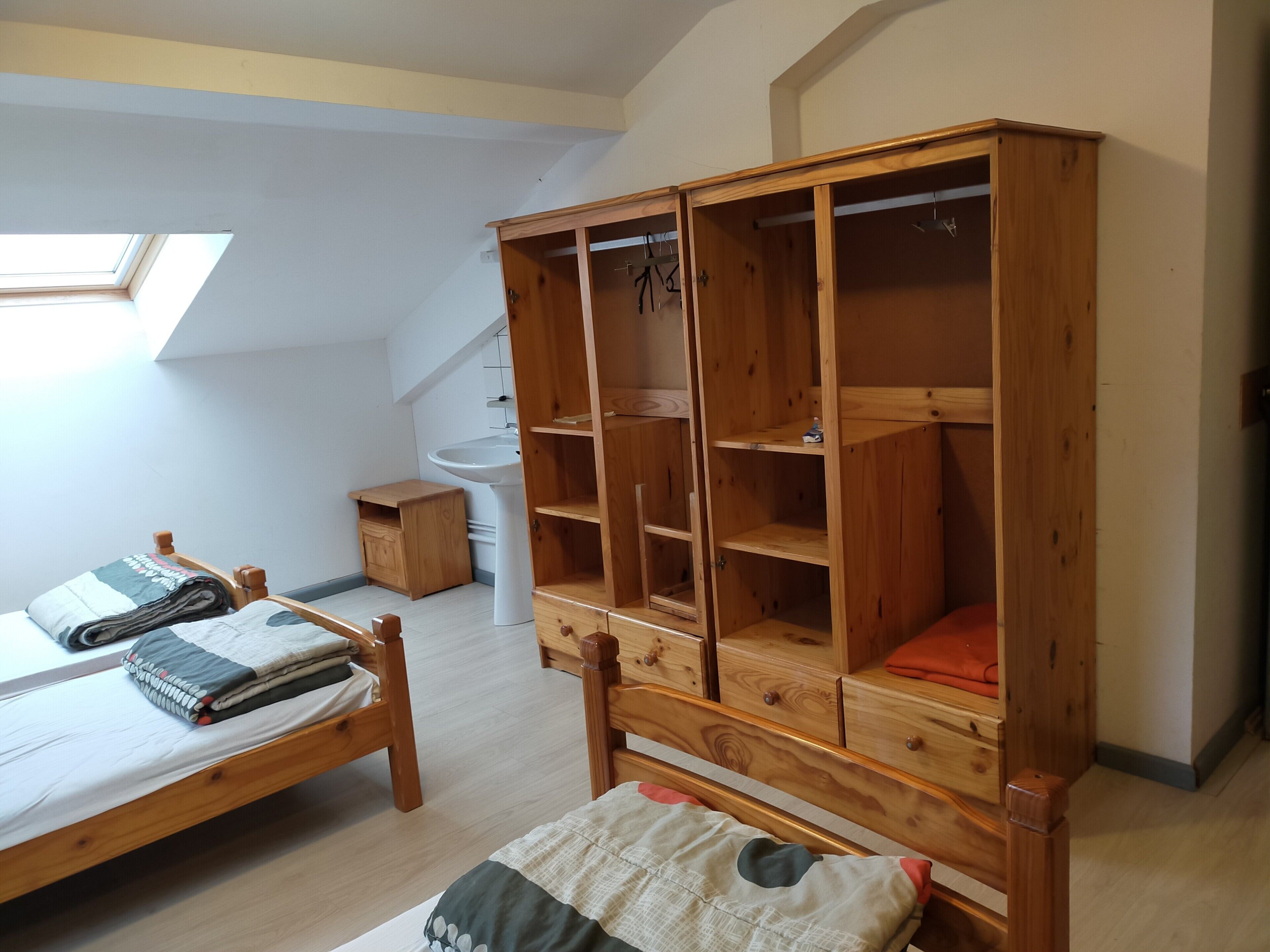 A bedroom with a wooden bed, a wooden wardrobe, a small bedside table, and a skylight.