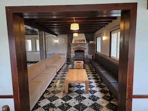Ein Zimmer mit Schachbrettmuster-Boden, einer Couch, einem Holztisch, einem Steinkamin und einem Holzbalken an der Decke.