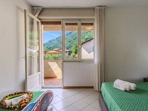 Ein Hotelzimmer mit einem Bett, einer grünen Decke, einem Handtuch, einem kissenförmigen Schlangenmotiv und Blick auf eine gebirgige Landschaft durch ein großes Fenster.