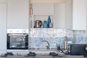 Eine moderne Küche mit weißen Schränken, einem eingebauten Backofen, einer gefliesten Spritzschutzleiste und einer Arbeitsplatte mit verschiedenen Küchenutensilien.