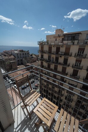 Un edificio alto con varios balcones, un banco de madera y vista al mar.