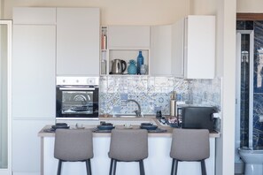 Una cocina compacta con armarios blancos, horno empotrado, lavabo y salpicadero de azulejos.