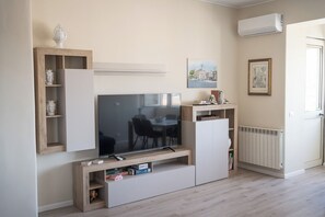 Ein modernes Wohnzimmer mit Flachbildfernseher, Regalen, Heizkörper und einer Tür.