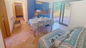 Una cocina compacta con armarios azules, una mesa de comedor preparada para cuatro personas y un ventanal corredero que da a un espacio exterior.