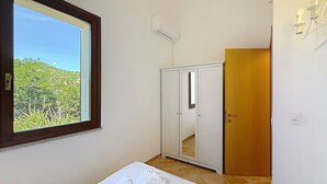 Una habitación con cama, armario, puerta y ventana con vista a follaje.