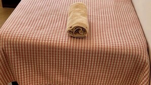 Una cama bien hecha con una colcha a cuadros y una toalla enrollada encima.