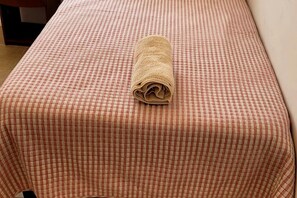 Una cama bien hecha con una colcha a cuadros y una toalla enrollada encima.