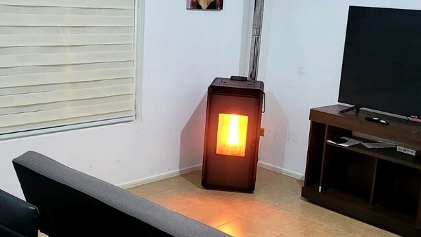 Una habitación con televisión sobre un mueble de madera, un calentador, un banco y una ventana con persianas.