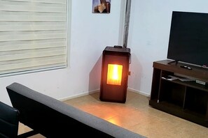 Quarto com televisão sobre suporte de madeira, aquecedor, banco e janela com persianas.
