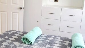 Una habitación con cama, cómoda blanca con cajones y una puerta.