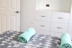 Una habitación con cama, cómoda blanca con cajones y una puerta.