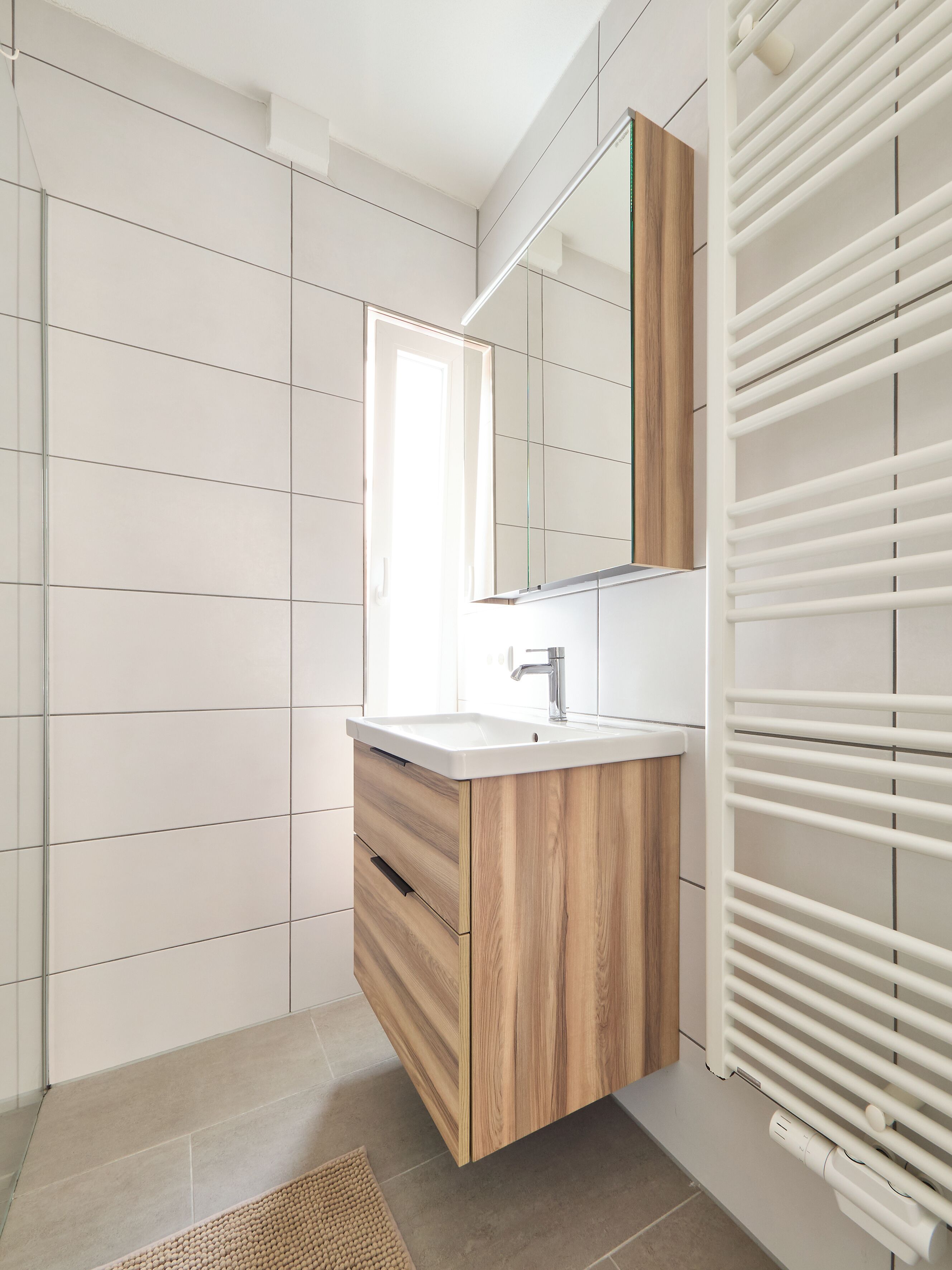 Een moderne badkamer met een houten wastafelmeubel, een spiegel en een witte radiator.