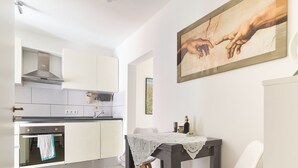 A modern kitchen with white cabinets, a dining table with chairs, and a painting on the wall. - Cozy little apartment with e-bike charging station; motorcyclists welcome (Glattbach)