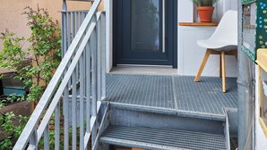 A modern building with a dark door, a small potted plant, and a white chair outside. - Cozy little apartment with e-bike charging station; motorcyclists welcome (Glattbach)