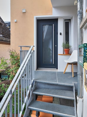 A modern building with a dark door, a small potted plant, and a white chair outside.