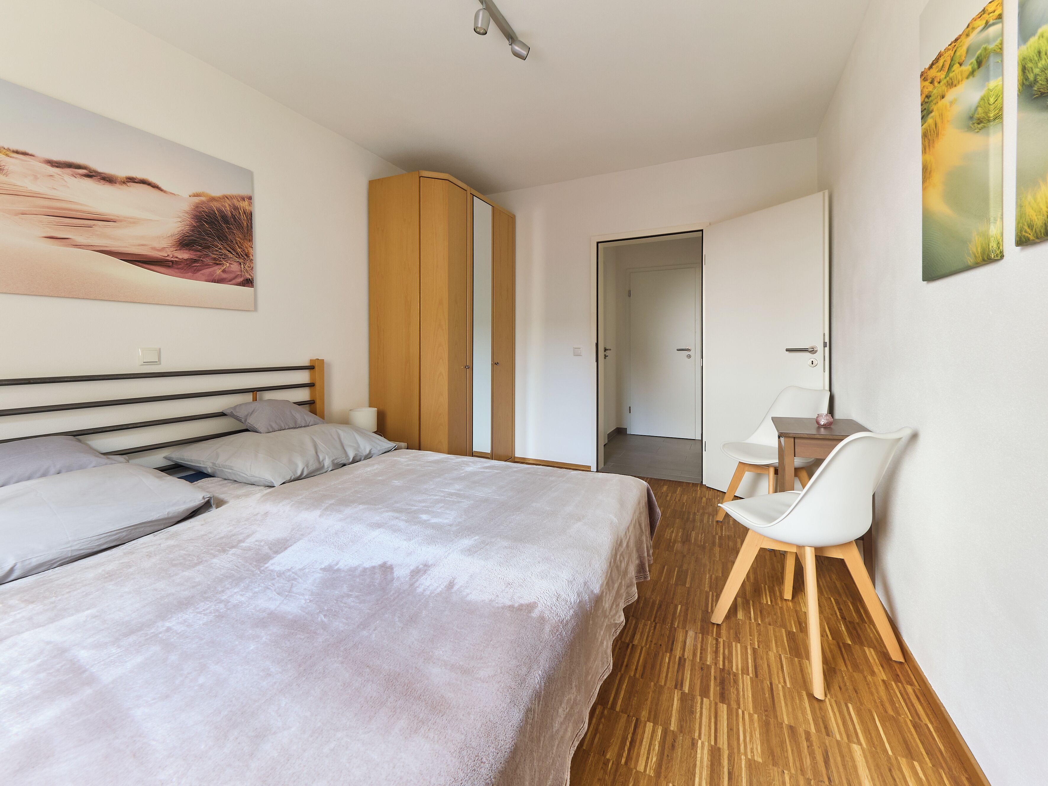 A bedroom with a bed, a chair, a wardrobe, and a door leading to another room.