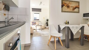 A modern kitchen with a dining area, a painting on the wall, and a view into the living room. - Cozy little apartment with e-bike charging station; motorcyclists welcome (Glattbach)