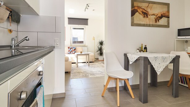 Eine moderne Küche mit Essbereich, einem Gemälde an der Wand und Blick in das Wohnzimmer.