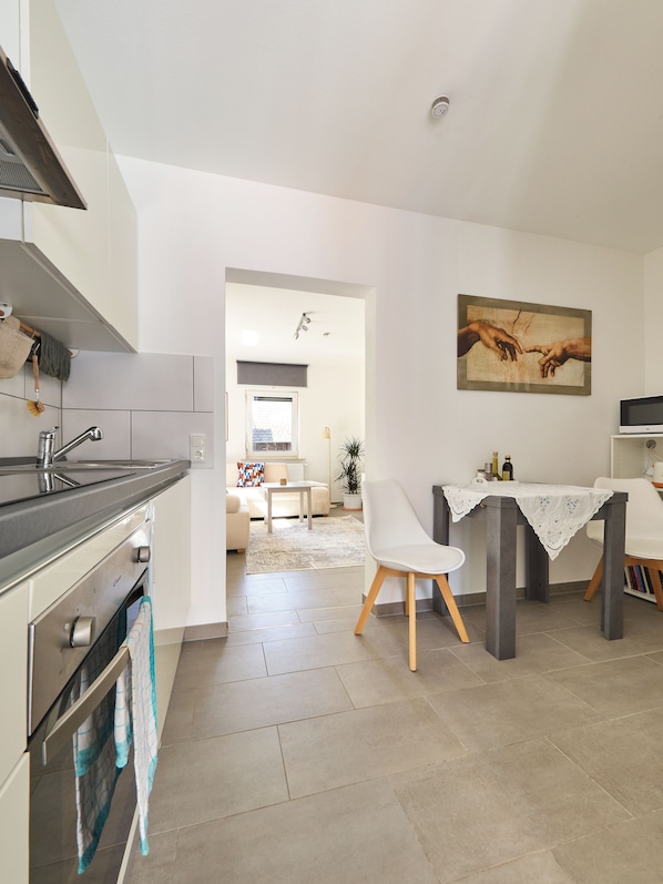 A modern kitchen with a dining area, a painting on the wall, and a view into the living room.