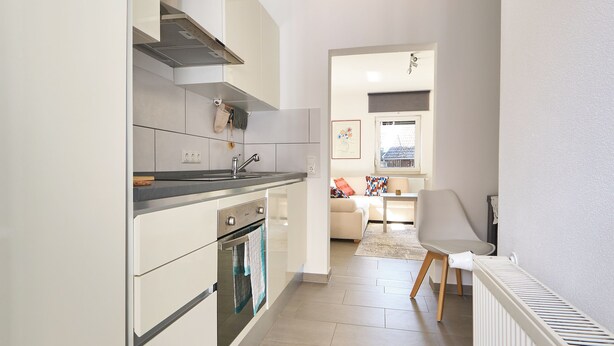 A modern kitchen with white cabinetry, a built-in oven, and a dining area with a table and chairs. - Cozy little apartment with e-bike charging station; motorcyclists welcome (Glattbach)