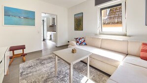 A modern living room with a sofa, a coffee table, and a rug. There is a window with a view of a building outside. - Cozy little apartment with e-bike charging station; motorcyclists welcome (Glattbach)