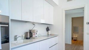 Eine moderne Küche mit weißen Schränken, einer Edelstahl-Spüle, einer Kaffeemaschine und einem Wasserkocher.