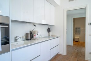 Eine moderne Küche mit weißen Schränken, einer Edelstahl-Spüle, einer Kaffeemaschine und einem Wasserkocher.