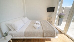 Ein modernes Schlafzimmer mit einem Bett, einem Flachbildfernseher, einem kleinen Tisch und einer Topfpflanze.