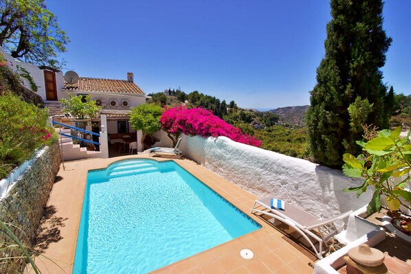 Una piscina con vista su un pendio, un muro in pietra e un edificio con tetto in tegole.