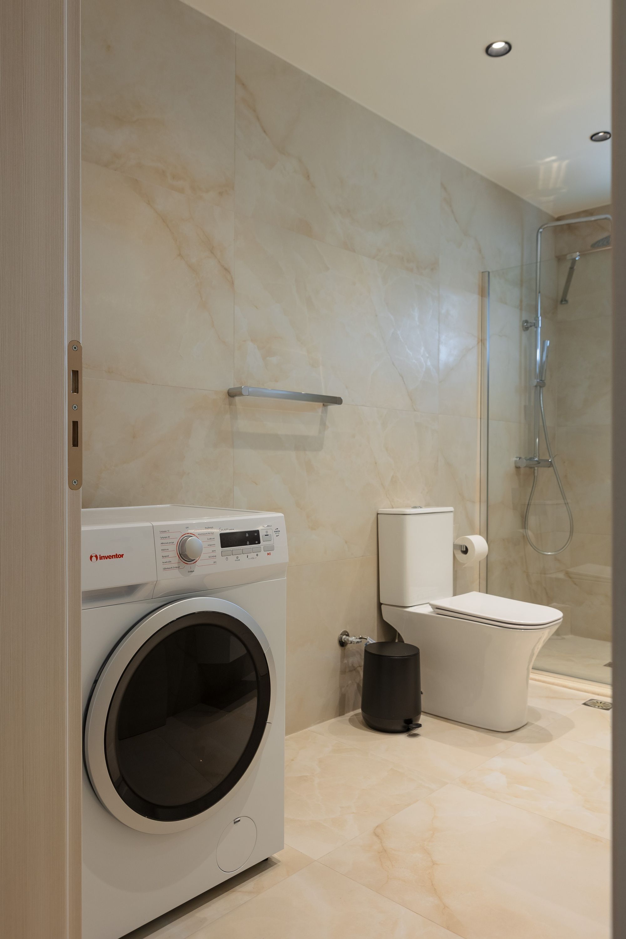 Une salle de bain moderne équipée d’un lave-linge, de toilettes et d’une douche.