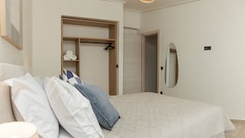 Een slaapkamer met een bed, kussens, een bedlampje, een houten garderobe, een spiegel en een hangende lamp.