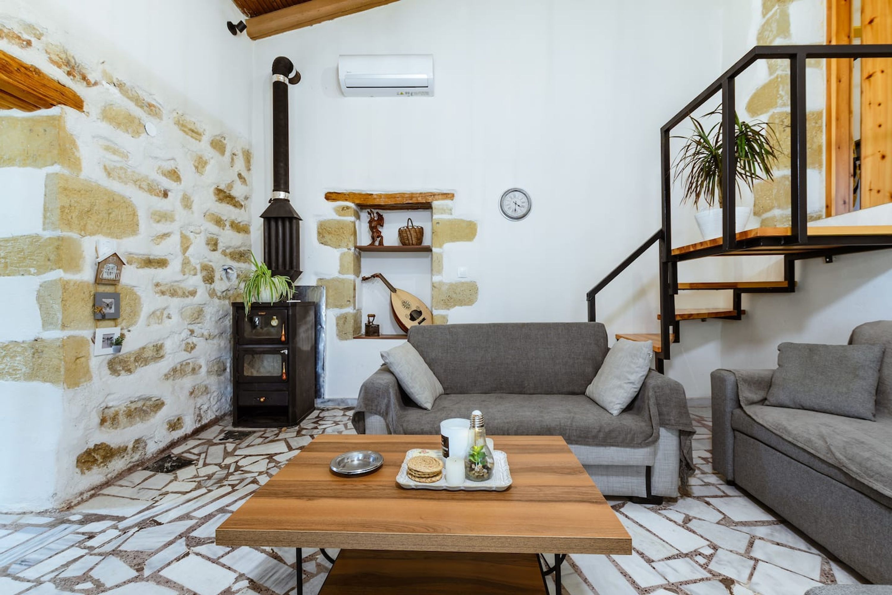 A cozy living room with a stone wall, a fireplace, a sofa, a coffee table, and a staircase.