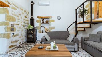 A cozy living room with a stone wall, a fireplace, a sofa, a coffee table, and a staircase.