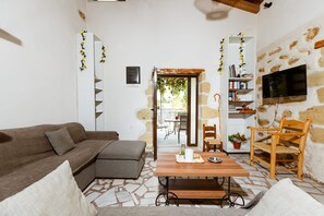 A living room with a sofa, a wooden table, a TV mounted on a stone wall, and a bookshelf. - Xanthippi's Traditional House in Pemonia (Pemonia)